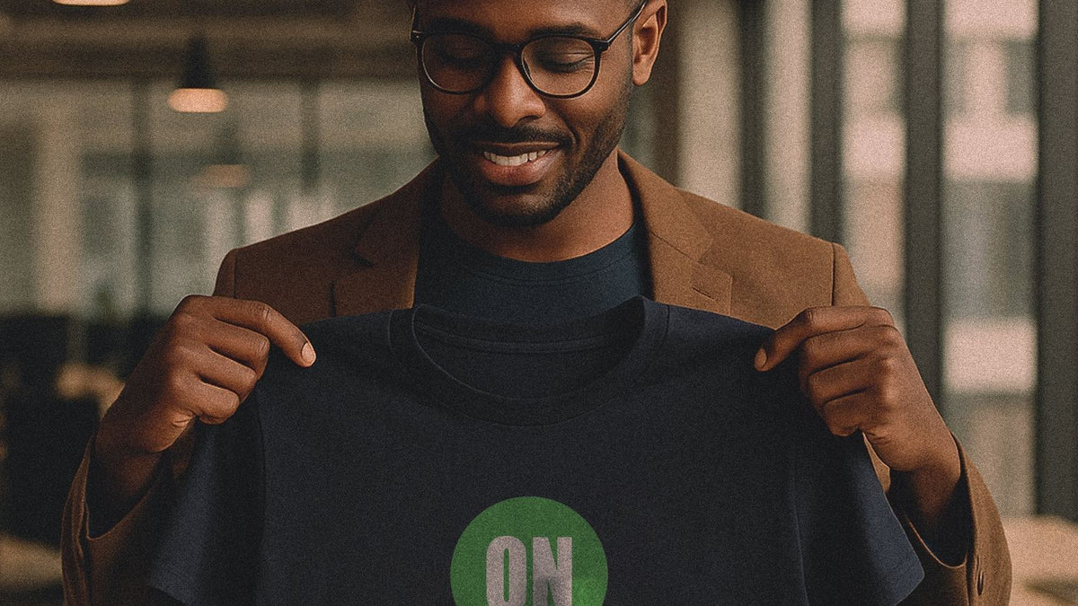 Smiling professional in a modern office holding up a navy screen printed team tee with a green logo