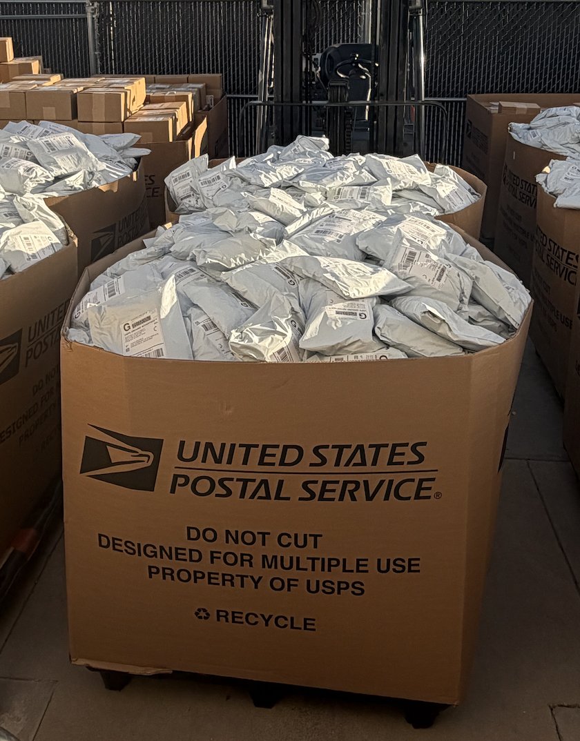 Mail bins full of packed and labeled poly mailers staged for USPS pickup at the Superluxe shop