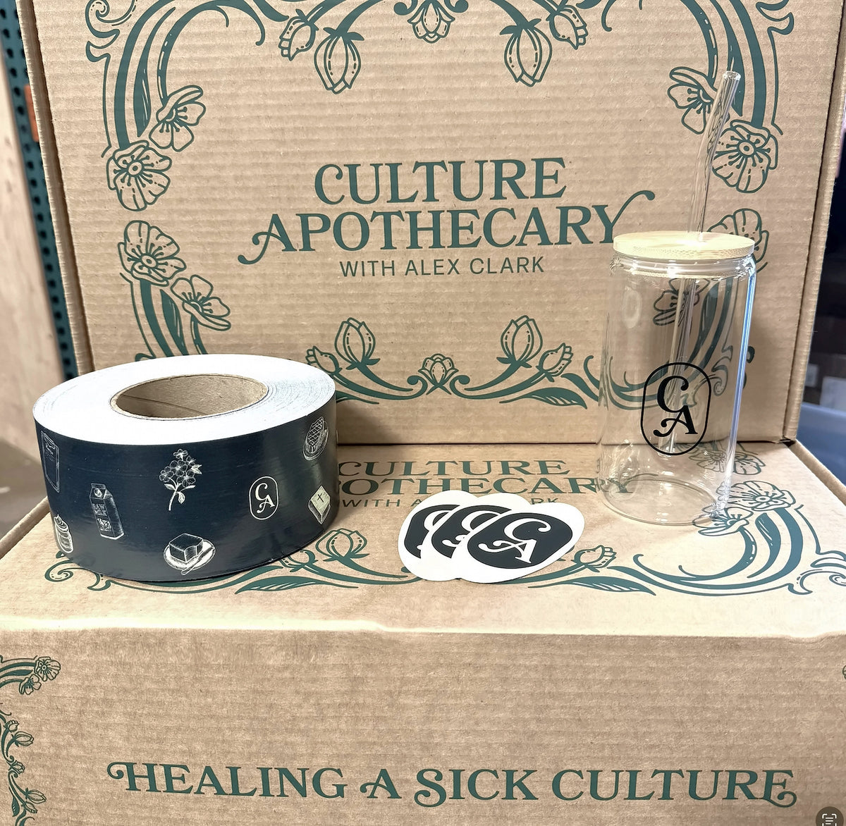 Culture Apothecary merch kit: custom printed shipping boxes shown with tape, stickers and a glass tumbler