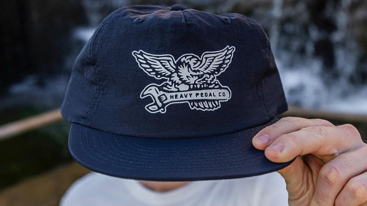 Hand holding a navy nylon cap decorated with a crisp white eagle and wrench heat transfer graphic