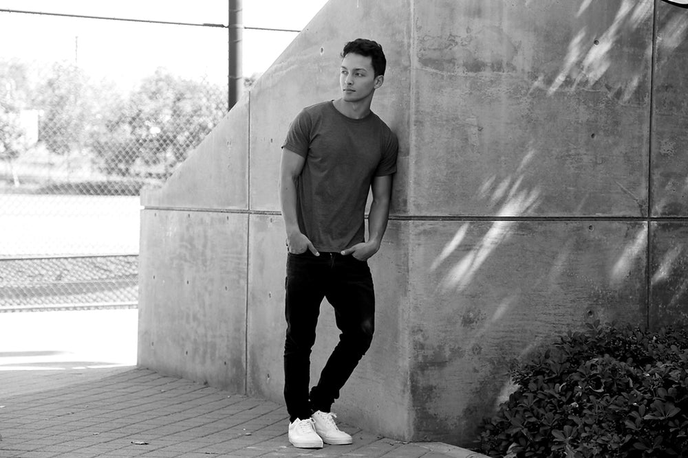 Man in a Bayside USA-made tee leaning on a concrete wall