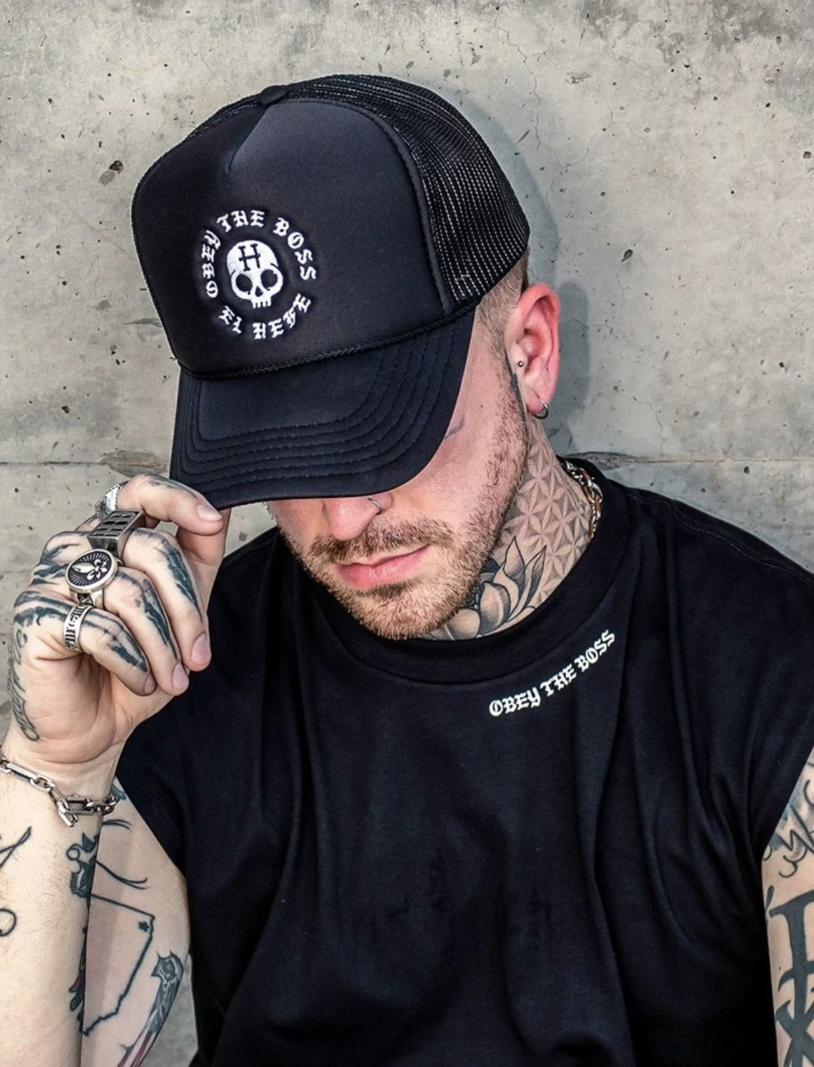 Tattooed man in a black trucker hat and tank top with custom branded apparel