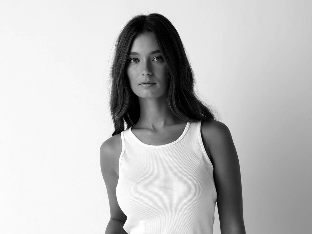 Woman in a white rib tank against a plain backdrop