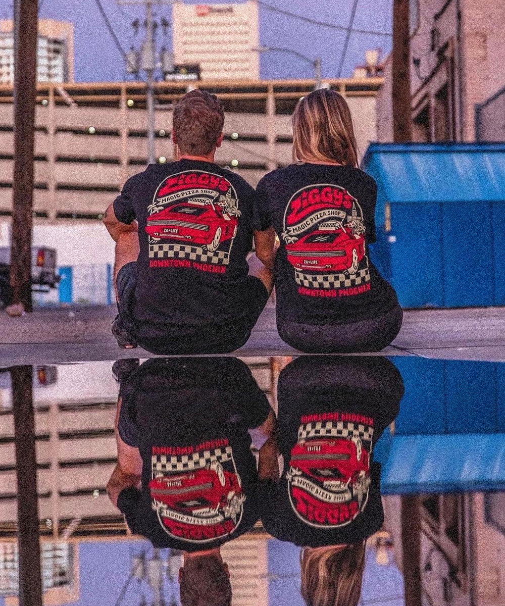 Two people seen from behind in matching black tees printed with a Ziggy's Magic Pizza Shop, Downtown Phoenix graphic