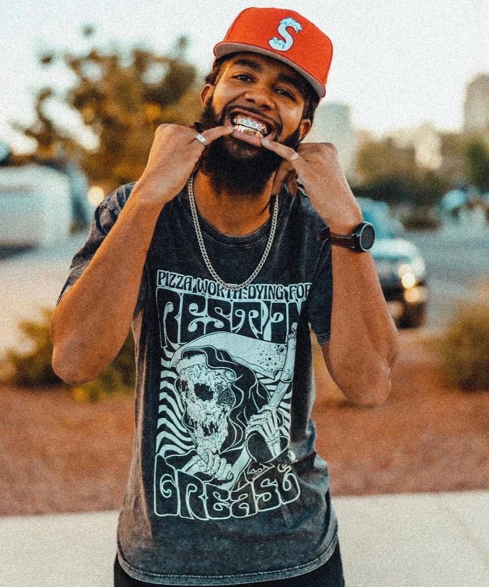 Smiling man in an orange cap and a custom-printed "Rest in Grease" graphic t-shirt