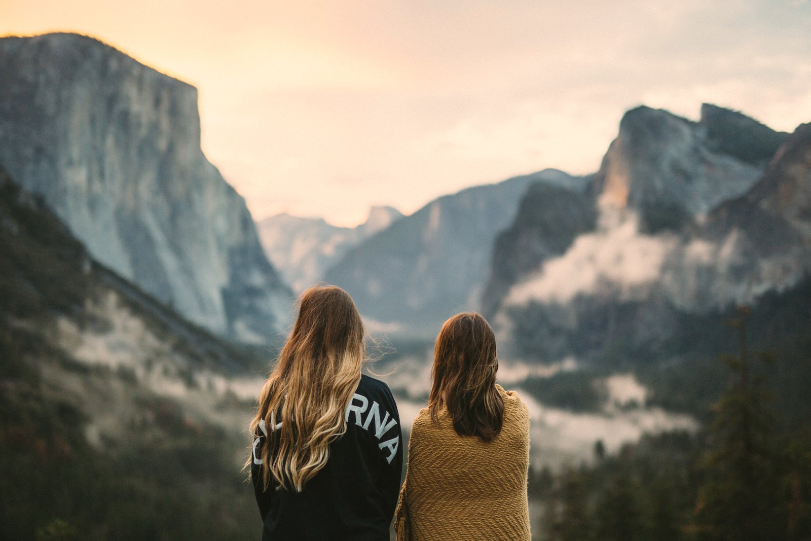 Wanderist mood photo: two friends looking out over Yosemite Valley at sunrise