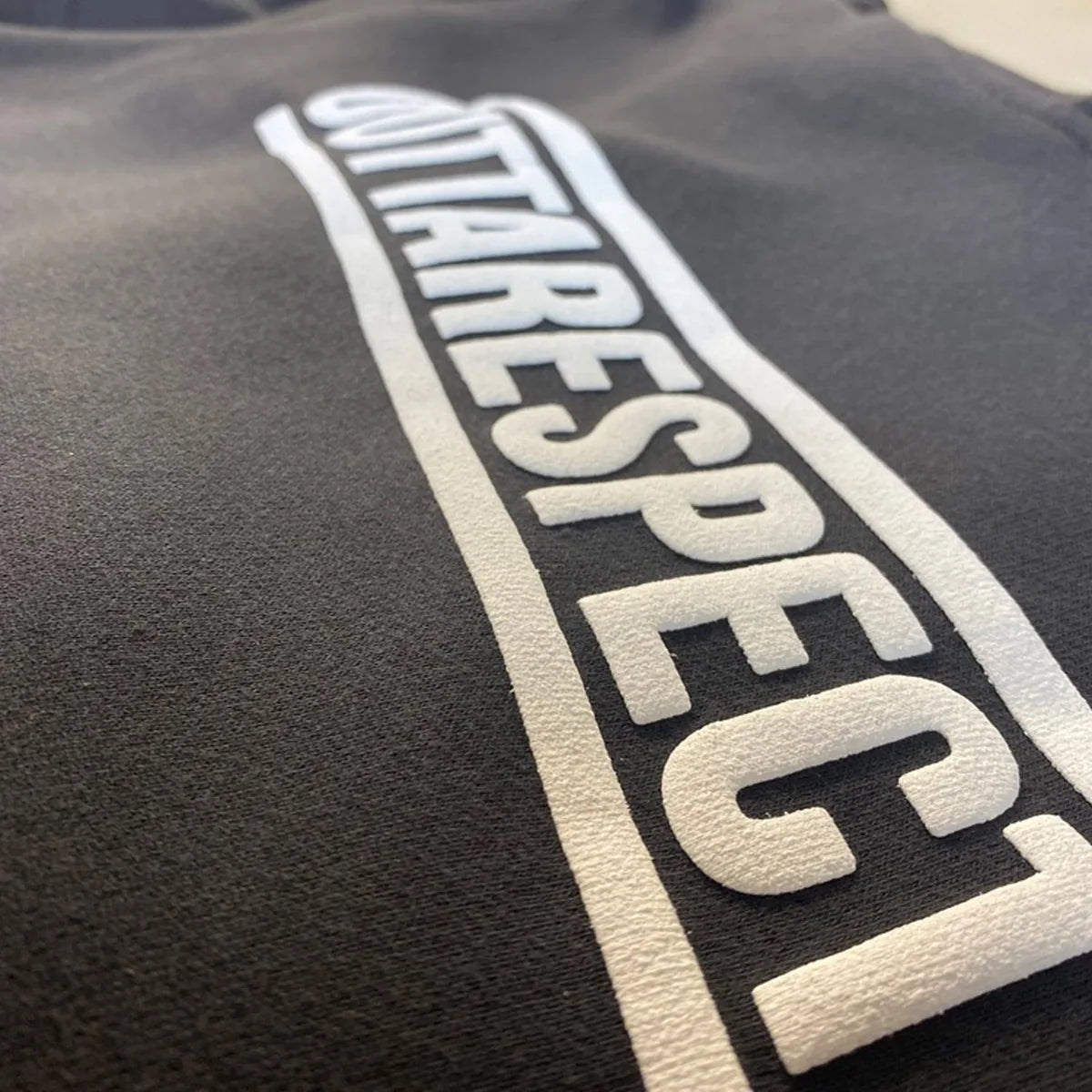 Close-up of raised white puff ink lettering printed on a black fleece sweatshirt